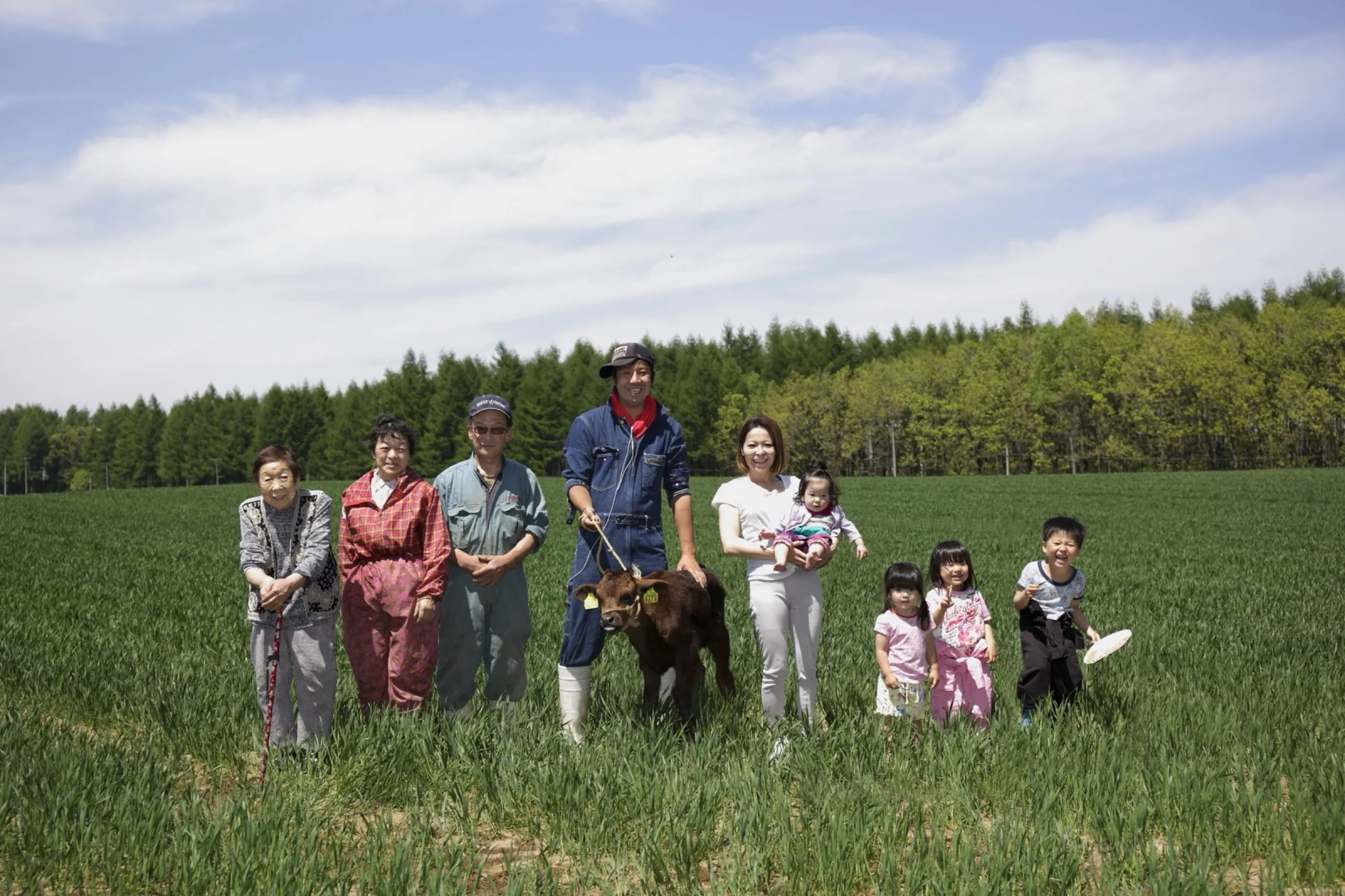 麦畑に立つ松橋農場の三世代と子牛